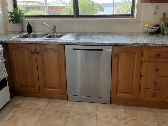 Built-in dishwasher under a kitchen bench beside a sink and wooden cabinets in Fullerton Cove