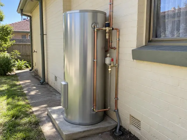 Stainless steel hot water system beside a cream brick wall and window on a concrete pad in Stockton