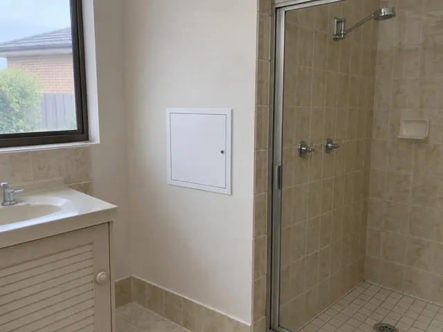 Bathroom wall with a small access panel beside a tiled shower and vanity in Fern Bay